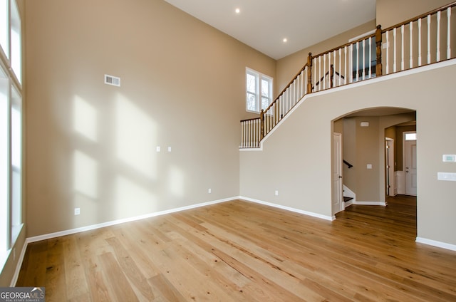 8555 Scenic Ridge Way, Ball Ground, GA 30107 - unfurnished living room featuring stairway, arched walkways, wood finished floors, a towering ceiling, and baseboards