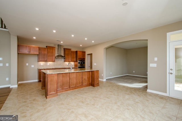 8555 Scenic Ridge Way, Ball Ground, GA 30107 - kitchen with wall chimney range hood, arched walkways, brown cabinetry, light stone countertops, and recessed lighting
