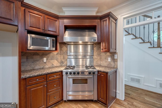 5620 Barnett Shoals Rd, Athens, GA 30605 - kitchen featuring appliances with stainless steel finishes, wall chimney range hood, light wood finished floors, tasteful backsplash, and stone counters
