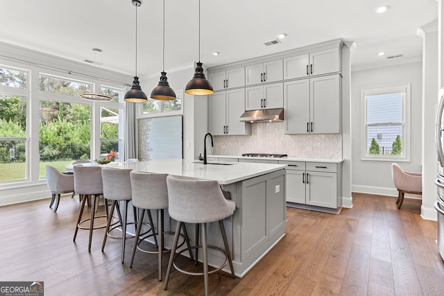 229 Widener Way, Peachtree City, GA 30269 - kitchen with under cabinet range hood, stainless steel gas stovetop, light countertops, light wood-style flooring, and decorative backsplash
