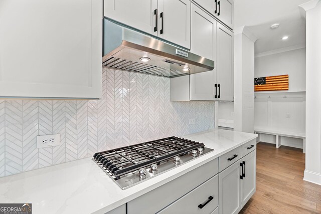 229 Widener Way, Peachtree City, GA 30269 - kitchen with under cabinet range hood, stainless steel gas cooktop, ornamental molding, tasteful backsplash, and light stone countertops