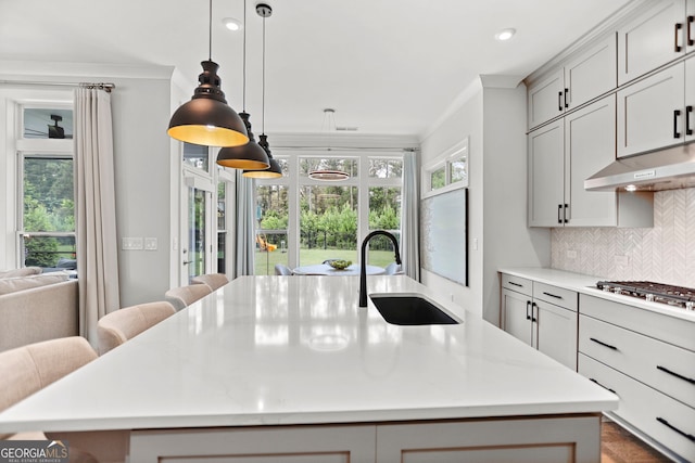 229 Widener Way, Peachtree City, GA 30269 - kitchen with under cabinet range hood, an island with sink, stainless steel gas stovetop, decorative backsplash, and decorative light fixtures