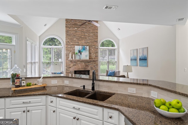 10630 N Edgewater Pl, Johns Creek, GA 30097 - kitchen with vaulted ceiling, a sink, dark stone countertops, white cabinets, and a fireplace