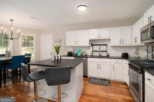 1478 Interlaken Pass, Jonesboro, GA 30238 - kitchen featuring appliances with stainless steel finishes, dark countertops, white cabinets, light wood finished floors, and a textured ceiling