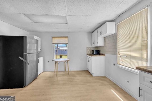 510 Edgewood Ave, Macon, GA 31201 - kitchen with freestanding refrigerator, white cabinetry, light wood-style flooring, a drop ceiling, and stacked washing machine and dryer