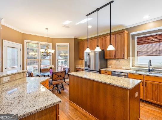 2810 Promenade Pl, Buford, GA 30519 - kitchen with appliances with stainless steel finishes, a center island, a sink, brown cabinetry, and ornamental molding