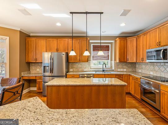 2810 Promenade Pl, Buford, GA 30519 - kitchen featuring appliances with stainless steel finishes, a sink, ornamental molding, a center island, and light stone counters