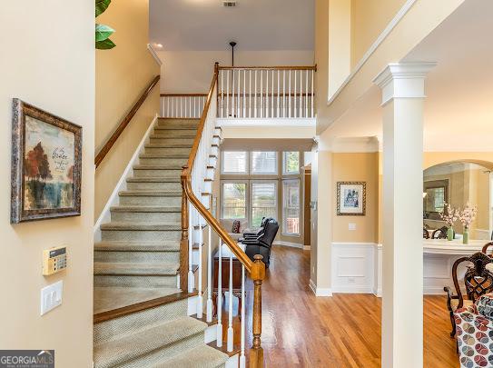 2810 Promenade Pl, Buford, GA 30519 - stairway with wood finished floors, a wainscoted wall, a towering ceiling, arched walkways, and a decorative wall