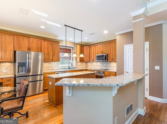 2810 Promenade Pl, Buford, GA 30519 - kitchen featuring appliances with stainless steel finishes, a kitchen island, a kitchen breakfast bar, brown cabinetry, and light stone counters