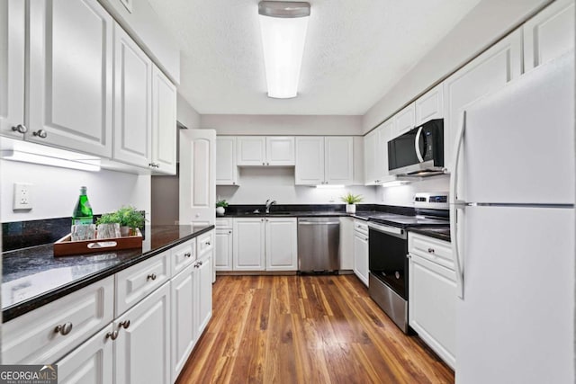 717 Beaufort Cir, Duluth, GA 30096 - kitchen with stainless steel appliances, a sink, white cabinets, dark countertops, and wood finished floors