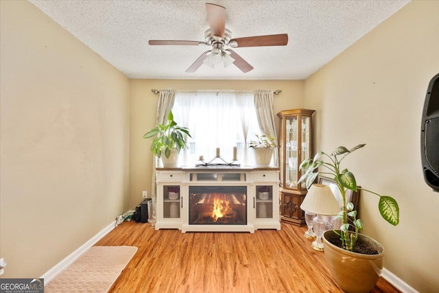 160 Country Mill Ln, Stockbridge, GA 30281 - living area with a textured ceiling, a ceiling fan, wood finished floors, a glass covered fireplace, and baseboards
