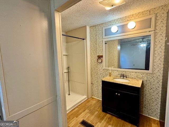 567 Anderson Parrish Rd, Portal, GA 30450 - bathroom featuring wood finished floors, a shower stall, wallpapered walls, vanity, and a textured ceiling