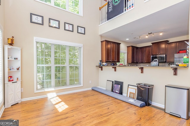 111 Portico Pl, Newnan, GA 30265 - kitchen with stainless steel microwave, a kitchen bar, fridge, light wood-style flooring, and baseboards