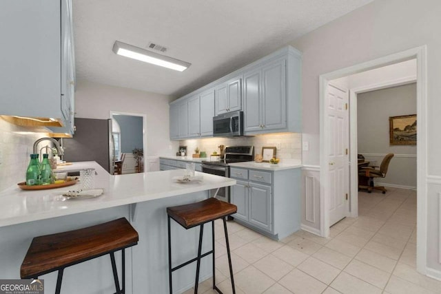 3027 Biltmore Woods Dr, Buford, GA 30519 - kitchen featuring appliances with stainless steel finishes, a peninsula, tasteful backsplash, light countertops, and a kitchen bar