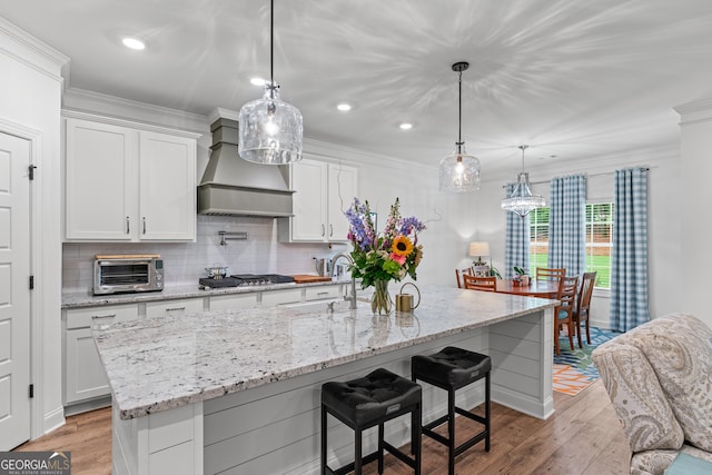 2036 Jefferson Hall Dr, Monroe, GA 30656 - kitchen with wall chimney range hood, white cabinetry, light wood finished floors, tasteful backsplash, and crown molding