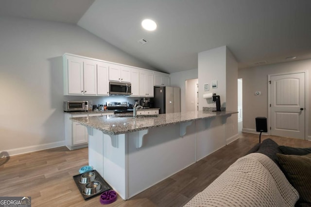 35 Westwood St, Danielsville, GA 30633 - kitchen with stainless steel appliances, lofted ceiling, a kitchen breakfast bar, light stone counters, and a peninsula