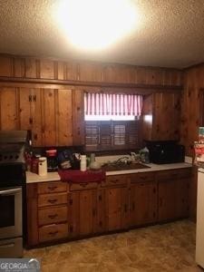 125 Jones St, Summerville, GA 30747 - kitchen featuring stainless steel electric range, a textured ceiling, brown cabinetry, a sink, and wooden walls