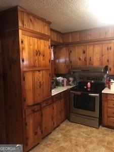 125 Jones St, Summerville, GA 30747 - kitchen featuring stainless steel electric stove, wooden walls, brown cabinets, under cabinet range hood, and light countertops