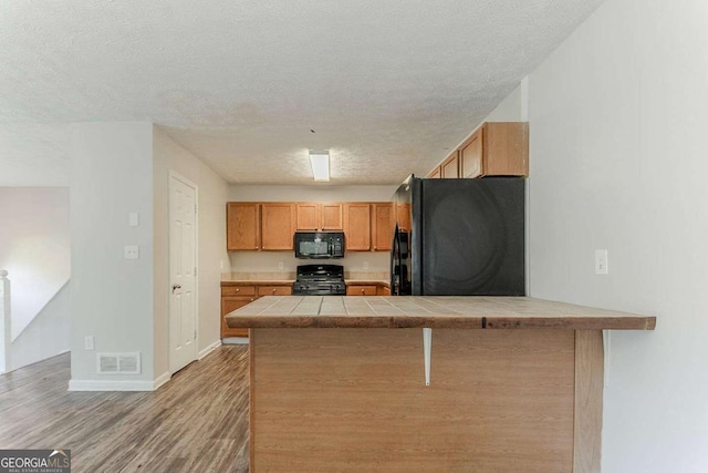 42 Breckenridge Dr, Powder Springs, GA 30127 - kitchen featuring black appliances, tile countertops, a peninsula, a textured ceiling, and light wood-style floors