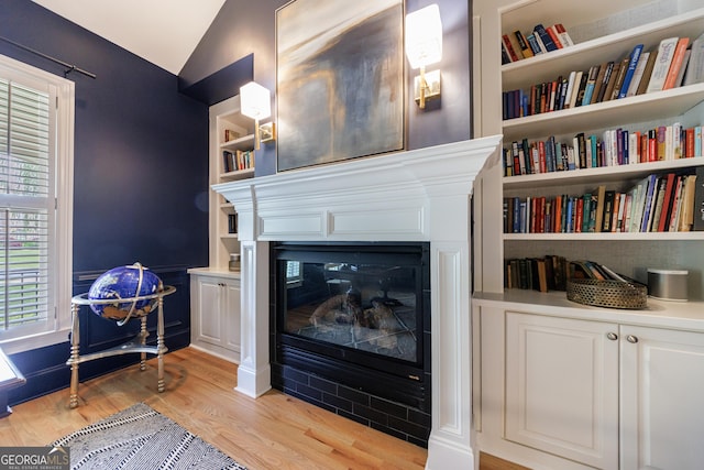 2101 Hunters Green Dr, Lawrenceville, GA 30043 - sitting room featuring light wood-style floors, lofted ceiling, a glass covered fireplace, and built in shelves