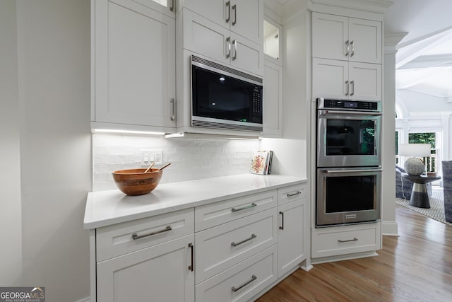 2101 Hunters Green Dr, Lawrenceville, GA 30043 - kitchen with stainless steel double oven, built in microwave, light wood-type flooring, decorative backsplash, and white cabinetry