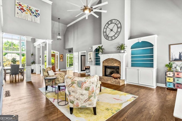 4251 Lantern Hill Dr, Dacula, GA 30019 - living area with high vaulted ceiling, a brick fireplace, ceiling fan, wood finished floors, and ornate columns
