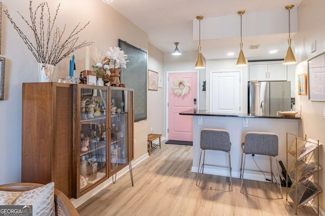 3040 Peachtree Rd NW Unit 1013, Atlanta, GA 30305 - kitchen featuring freestanding refrigerator, light wood-style flooring, a kitchen breakfast bar, white cabinets, and decorative light fixtures