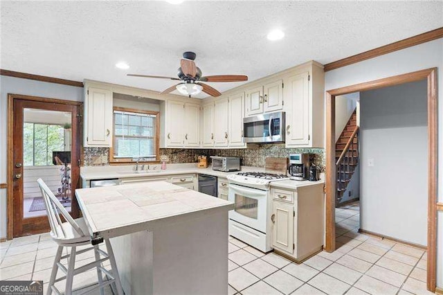 2041 Millspring Way NW, Kennesaw, GA 30152 - kitchen featuring stainless steel microwave, white range with gas cooktop, decorative backsplash, light countertops, and ornamental molding