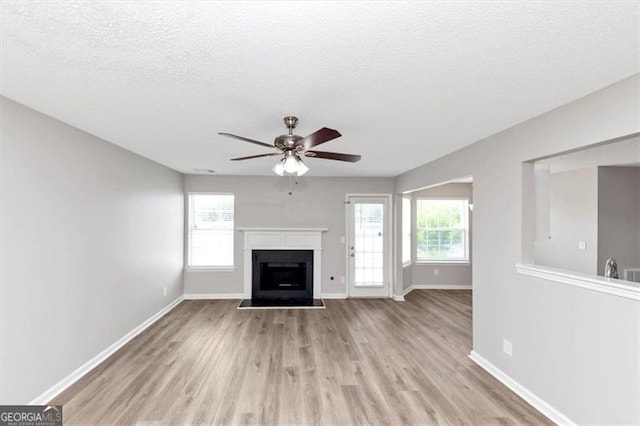 11827 Spring Lake Way, Fayetteville, GA 30215 - unfurnished living room with ceiling fan, light wood-style flooring, baseboards, a fireplace with raised hearth, and a textured ceiling