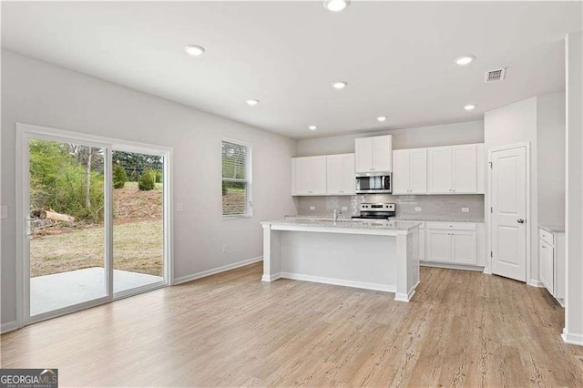 7193 Brushwood Bnd, Lithonia, GA 30058 - kitchen featuring stainless steel appliances, white cabinetry, backsplash, light wood-style flooring, and a kitchen island with sink