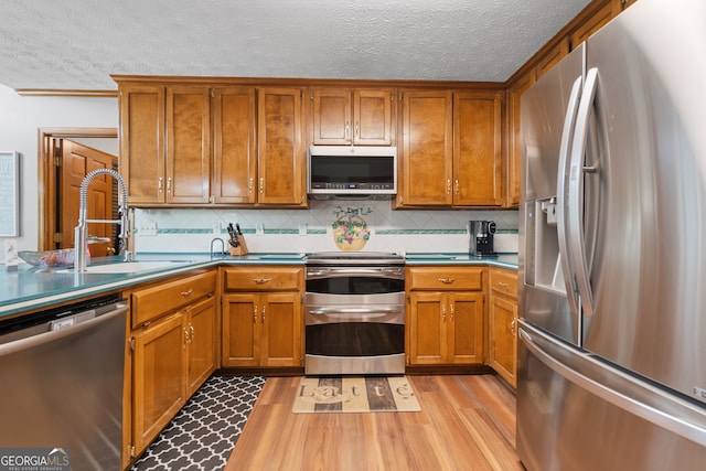 1850 Linnet Ct NE, Roswell, GA 30075 - kitchen featuring appliances with stainless steel finishes, brown cabinets, light wood finished floors, a sink, and a textured ceiling