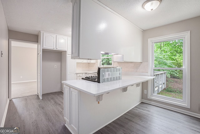 3006 Alberta Dr, Marietta, GA 30062 - kitchen featuring a textured ceiling, a peninsula, white cabinetry, light wood-style floors, and backsplash