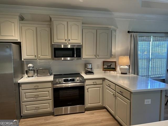 109 Berkley Cir, Warner Robins, GA 31093 - kitchen with appliances with stainless steel finishes, a peninsula, light countertops, light wood-style flooring, and ornamental molding