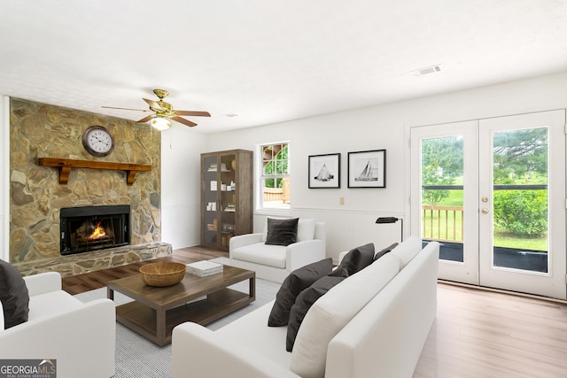 320 Edna Dr, Stockbridge, GA 30281 - living room featuring wood finished floors, french doors, a ceiling fan, a stone fireplace, and a wainscoted wall
