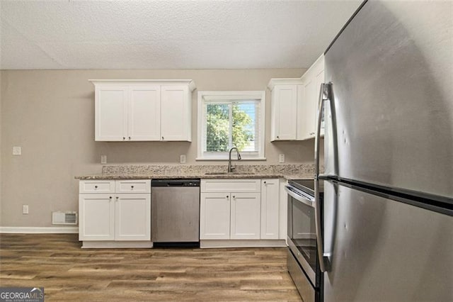 2641 Clifton Springs Rd, Decatur, GA 30034 - kitchen with appliances with stainless steel finishes, a sink, wood finished floors, white cabinetry, and light stone countertops