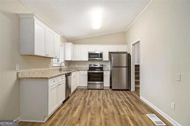 2641 Clifton Springs Rd, Decatur, GA 30034 - kitchen with stainless steel appliances, white cabinetry, lofted ceiling, light stone countertops, and light wood-style floors