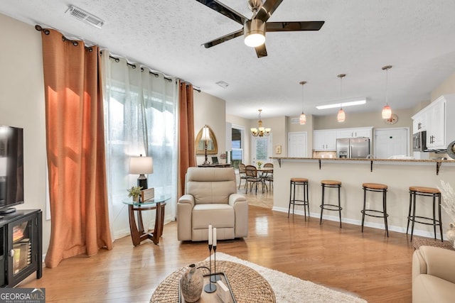 4174 Chatham Crest Ln, Buford, GA 30518 - living room featuring a chandelier, a ceiling fan, light wood finished floors, a textured ceiling, and baseboards