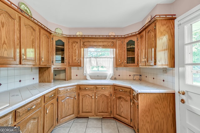 4911 Old Douglasville Rd, Lithia Springs, GA 30122 - kitchen with glass insert cabinets, tasteful backsplash, brown cabinetry, and light tile patterned flooring