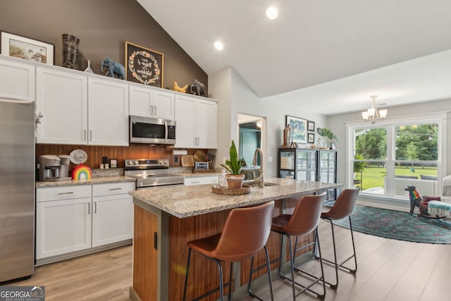 102 Bowline Ln, Kingsland, GA 31548 - kitchen featuring stainless steel appliances, white cabinetry, light wood-type flooring, a center island with sink, and light stone counters
