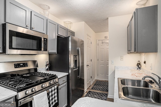 855 Lakeside Cir, Covington, GA 30016 - kitchen featuring stainless steel appliances, a sink, gray cabinetry, a textured ceiling, and light stone counters