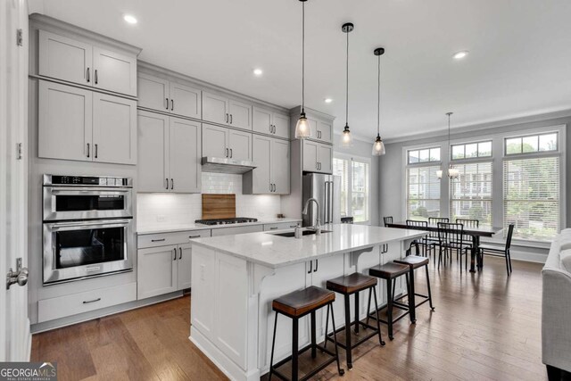3108 Huntington Pl, Milton, GA 30004 - kitchen featuring appliances with stainless steel finishes, a sink, backsplash, a kitchen bar, and a center island with sink