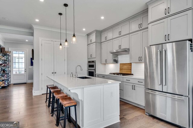 3108 Huntington Pl, Milton, GA 30004 - kitchen with appliances with stainless steel finishes, a sink, under cabinet range hood, ornamental molding, and a center island with sink