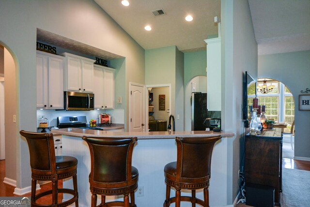 9013 Aldbury Dr, Locust Grove, GA 30248 - kitchen with stainless steel appliances, arched walkways, vaulted ceiling, white cabinets, and baseboards