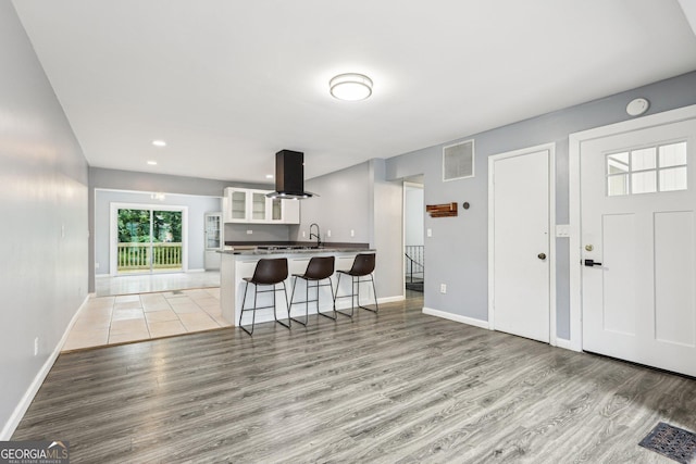 6072 Holiday Blvd, Forest Park, GA 30297 - kitchen featuring light wood-style flooring, a breakfast bar area, island exhaust hood, white cabinets, and glass insert cabinets