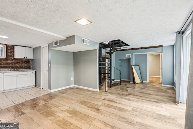 6072 Holiday Blvd, Forest Park, GA 30297 - unfurnished living room with stairs, a textured ceiling, baseboards, a sink, and light wood-style floors