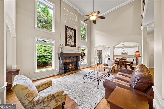 161 Highgrove Dr, Suwanee, GA 30024 - living room with arched walkways, a towering ceiling, ceiling fan, a lit fireplace, and light wood-style floors