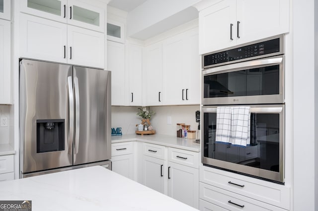 3537 Edenridge Ct, Buford, GA 30519 - kitchen featuring appliances with stainless steel finishes, white cabinetry, glass insert cabinets, tasteful backsplash, and light stone countertops