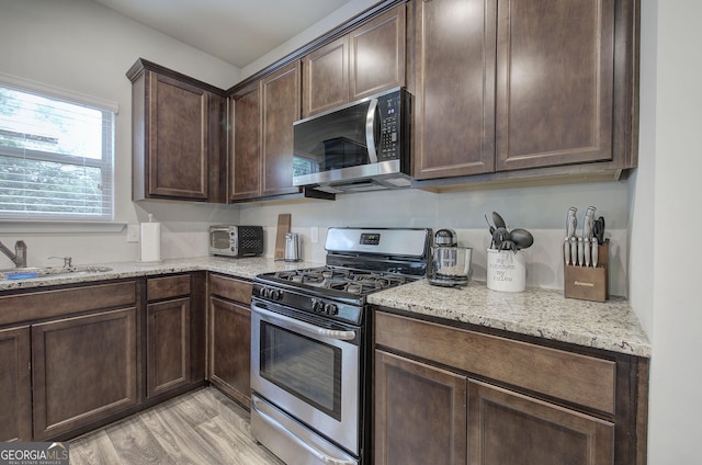 79 Mercer Ln, Cartersville, GA 30120 - kitchen featuring stainless steel appliances, a sink, dark brown cabinets, light wood finished floors, and light stone countertops