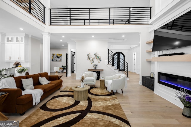2631 Sardis Way, Buford, GA 30519 - living area with a towering ceiling, light wood-style flooring, a glass covered fireplace, stairs, and decorative columns