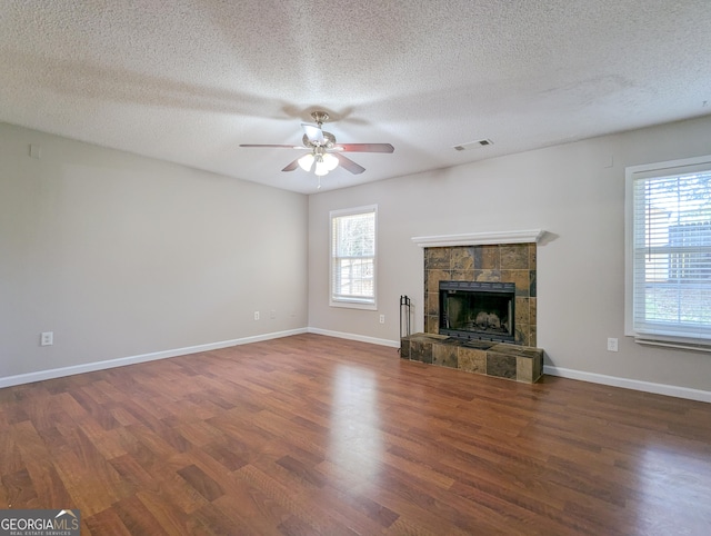 2918 Pavia Cir, Austell, GA 30106 - unfurnished living room with healthy amount of natural light, wood finished floors, ceiling fan, a tiled fireplace, and a textured ceiling